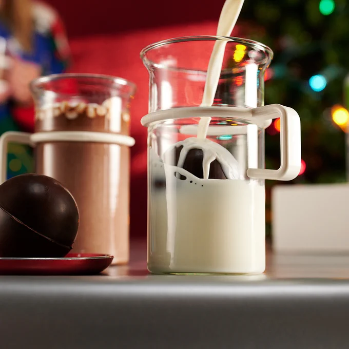 warm milk pouring over a hot chocolate bomb in a clear mug. The milk is melting the chocolate.