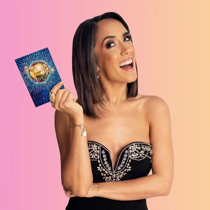 Janette Manrara stands smiling and holding a Strictly Come Dancing The Live Tour cue card.