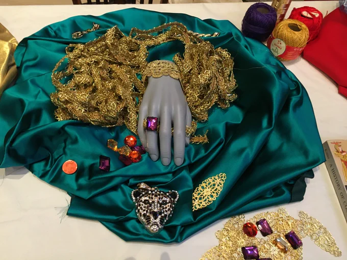 Piece of green cloth with fake jewels and some braid scattered around.