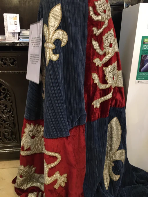 A cloak of red and blue fabric with gold lions and fleur de lys applique.