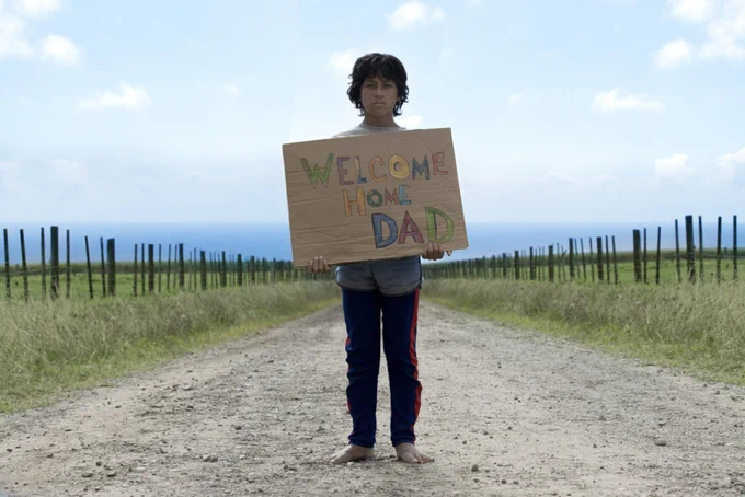 A boy holds up a homemade sign that says "Welcome home dad"