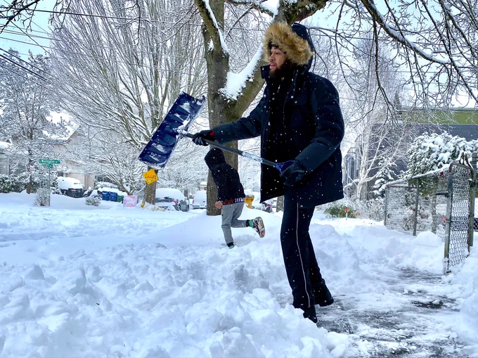 Man using a blue shovel for shoveling snow on ground out of yard. 
