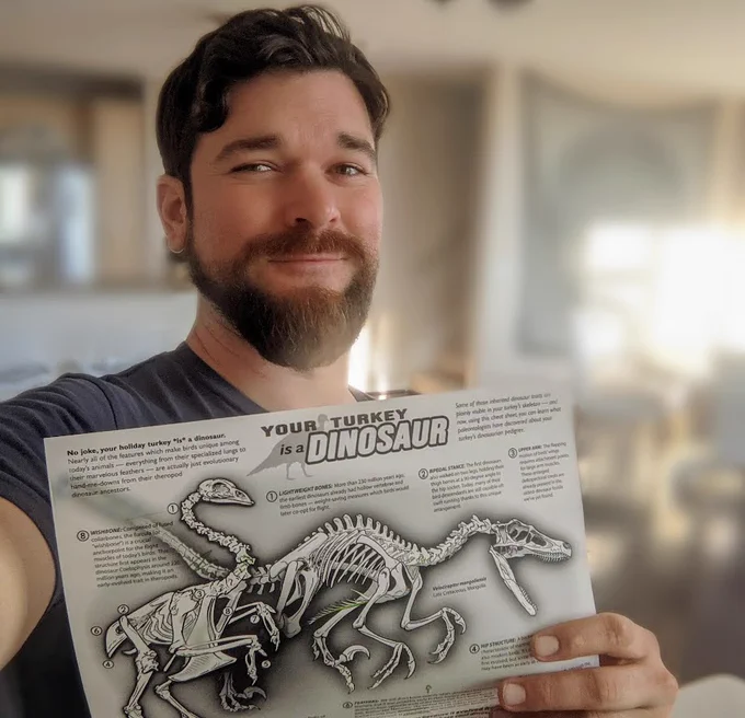 Danny Anduza holding a printed copy of the turkey and Velociraptor skeleton diagram