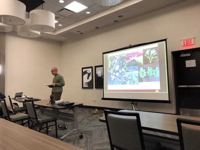Dr. Thomas Stefaniak in front of a presenter with pictures of a potato variety with its leaves and flowers also shown.