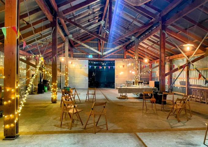 Cosy open-sided barn covered in fairy lights and multicoloured bunting, with seats laid out waiting for attendees to arrive