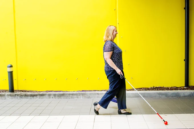 A woman with a white cane walking on the footpath. 