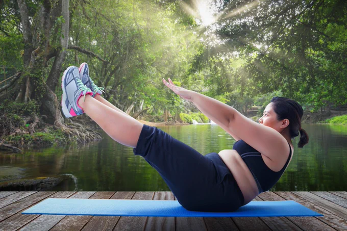 Woman exercising on a mat, on a wooden platform, overlooking a lake surrounded by trees.
