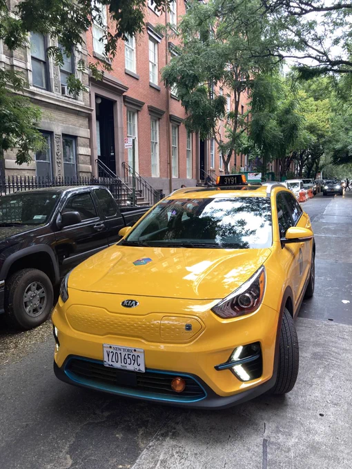 An Electric Taxi travels down a tree-lined street in Manhattan.