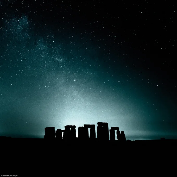 Stonehenge at night outlined in silhouette against a starry sky.