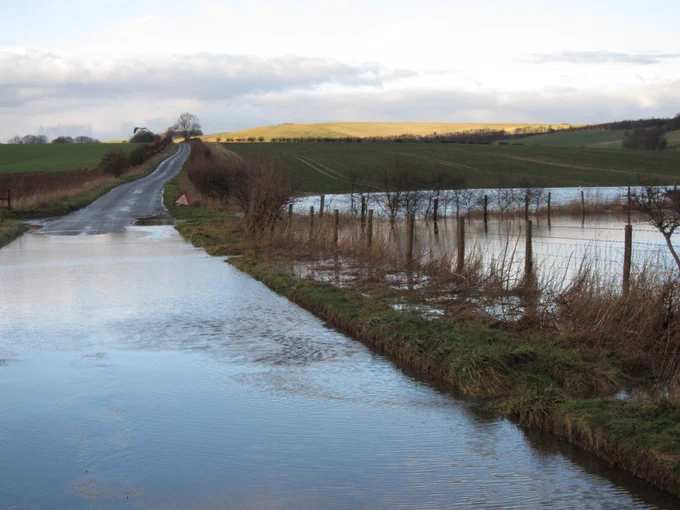 Groundwater flooding in Wiltshire. To the left is a road covered in water, on the right waterlogged fields. 