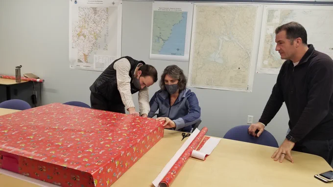 Three people wrapping Christmas presents.