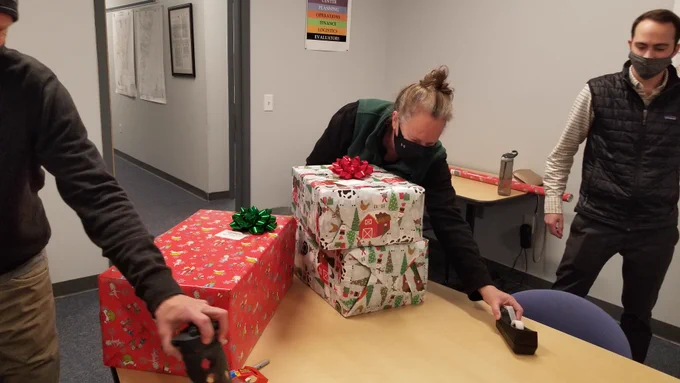 Three people wrapping Christmas presents.