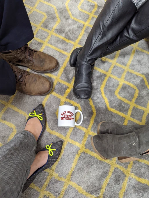 Feet and shoes on a carpet with an SDSU mug