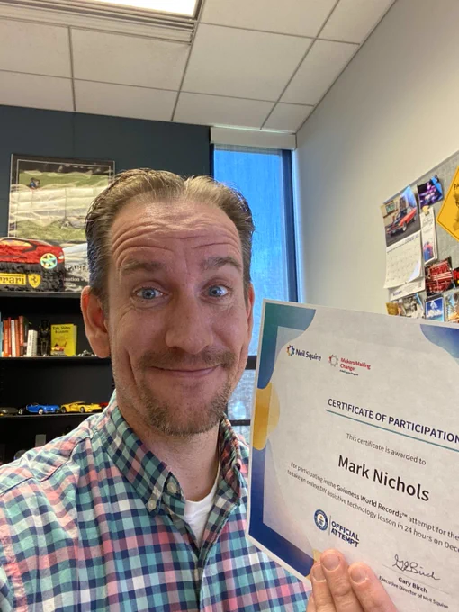 photograph of Mark Nichols within his office holding a Certification of Participation in the Guinness World Records attempt for the online DIY assistive technology lesson within 24 hours on December 3, 2021. 