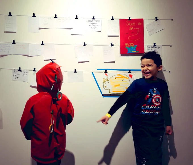 Two children, one facing the camera, in a gallery with cards clipped to the wall