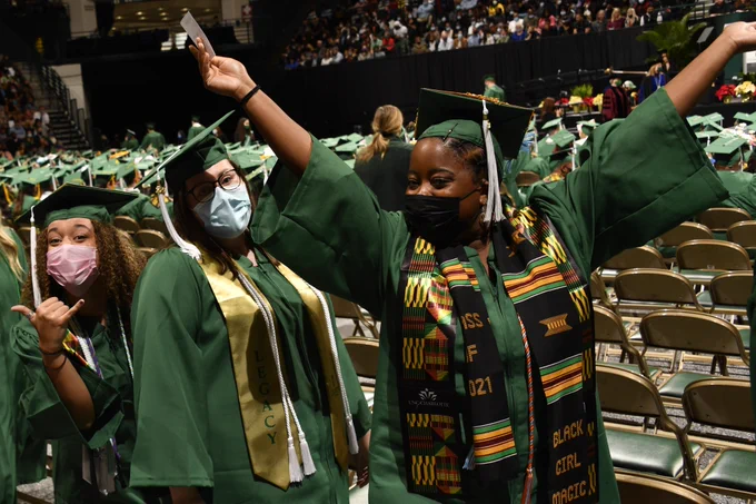 A group of three graduates lining up to cross the stage in Halton Arena. 