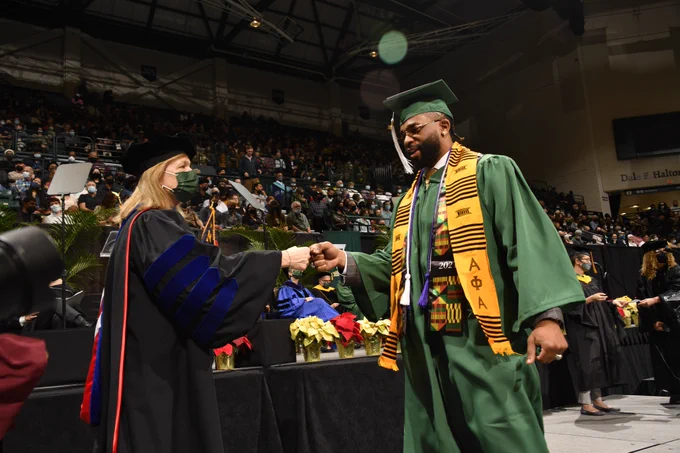 A graduate giving Chancellor Gaber a fist bump as they cross the graduation stage in Halton Arena. 