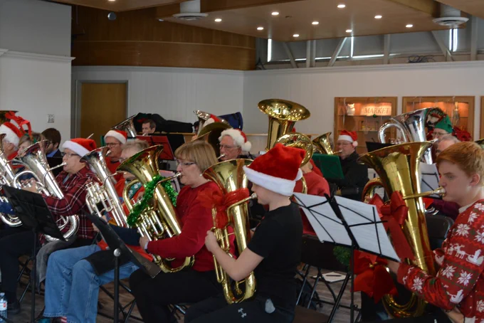 A large group of people playing tuba and euphonium wearing festive clothing, Santa hats, and with decorated instruments. Image taken in December 2019.