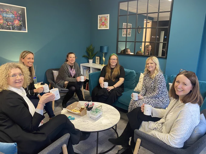 Photo shows attendees of a training course having a tea break and sitting in a circle on sofas.