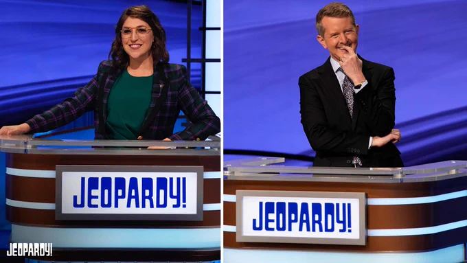 Mayim Bialik and Ken Jennings stand at the Jeopardy! host lectern. 