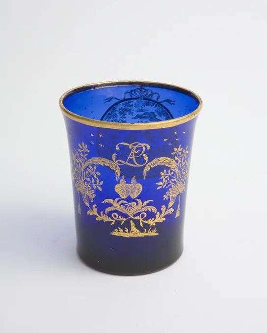 Blue glass drinking glass with gilded design of interlocking hearts and a bird. 