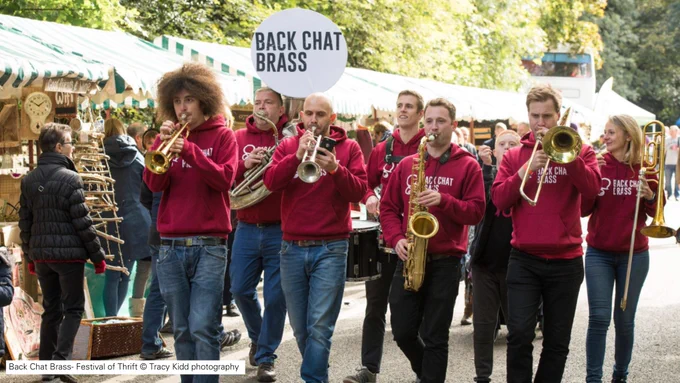 "Back Chat Brass" walking through market streets playing instruments all wearing red hoodies 