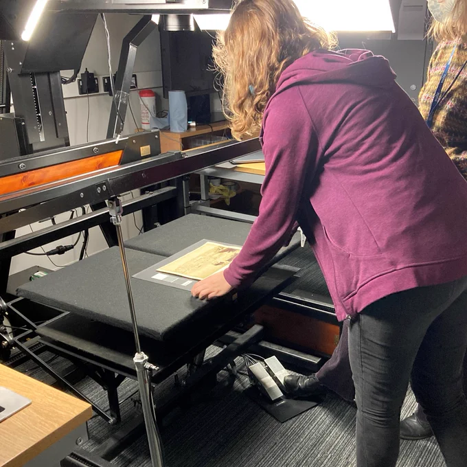 One of the digital humanities interns and technical assistant placing an archived photograph under the glass cover of a large copystand for photography