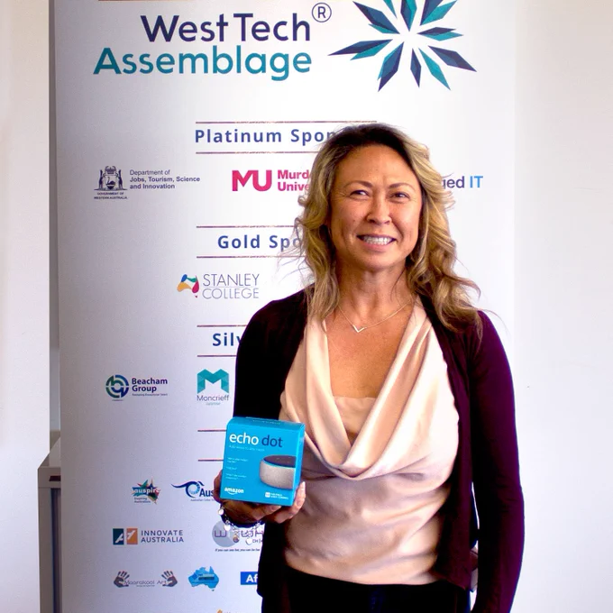 Susanne Staton smiling and holding her Amazon Echo Dot prize in front of a West Tech Assemblage 2021 banner.