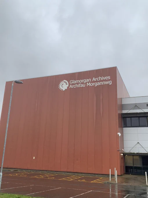 Grey sky in front of which is the large brown coloured wall of a building that white writing tells you (in English and Welsh) is Glamorgan Archives