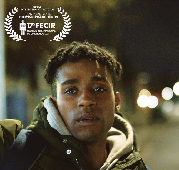 Film still of a young Black man looking longingly into the distance. Top left a winning laurel for best actor