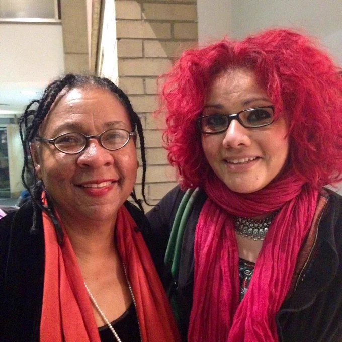 Mona and bell standing together from the shoulders up, wearing black tops