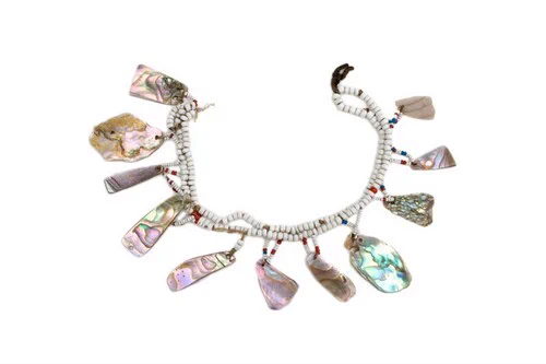 Een ketting met vooral witte, maar ook enkele rode en blauwe kralen. Aan de ketting hangen rechthoekige en driehoekige stukken abalone, een glimmende schelp.
