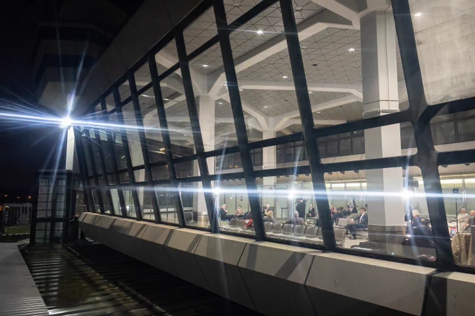 Blick bei Nacht von außen durch eine erleuchtete Fensterfront am Flughafen Tegel; innen sitzen in einer ehemaligen Wartehalle Menschen bei einer Veranstaltung