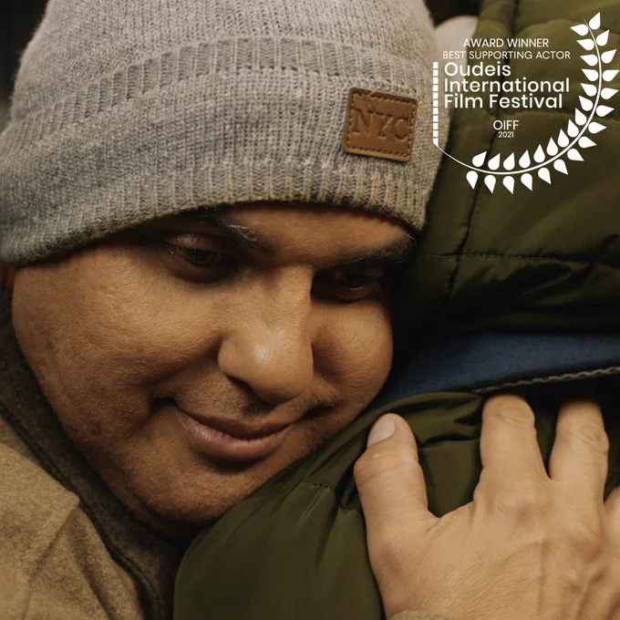 Close up on the face of a middle aged Hispanic man hugging someone. Winning film festival laurel in the top right corner.​