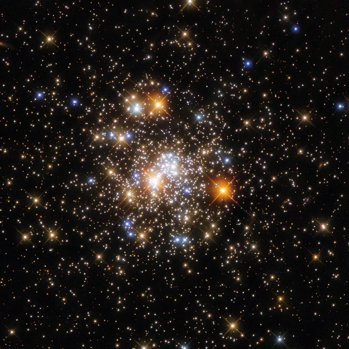 Cluster of stars in varying shapes and sizes. Red giants are seen among smaller stars speckled throughout the image. They appear as bright lights,  almost like fireworks.