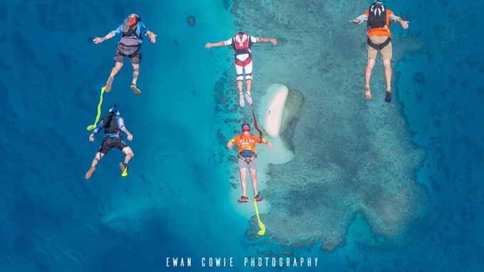 five skydivers tracking over turquoise coloured ocean and tropical island