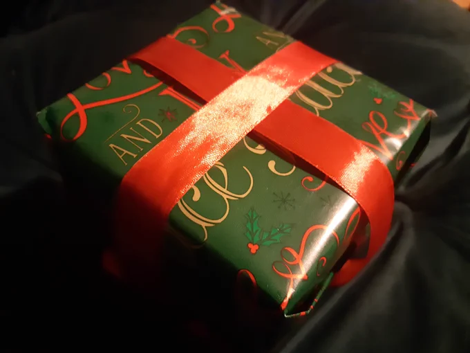 A Christmas gift wrapped in green, red and gold paper with a red ribbon