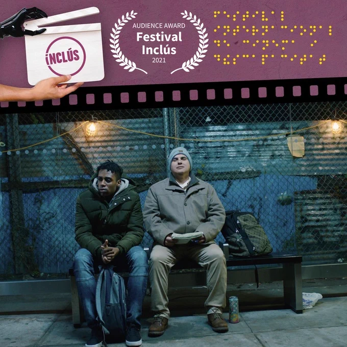 Film still of a young Black man seated next to a middle aged Hispanic man at a bus stop. Top left reads "Inclus," top middle is a winning film festival laurel for the audience award, top right are braille dots
