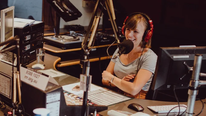 Monique Sebire behind the Triple R studio panel, wearing headphones and smiling.