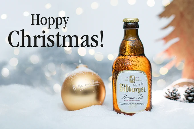 Bitburger Premium Pils im Schnee mit einer goldenen Bitburger Weihnachtskugel. 