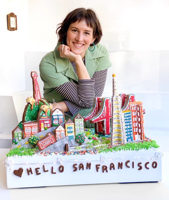 a display of san francisco landmarks made completely out of gingerbread, icing, and candy with the creator in the background