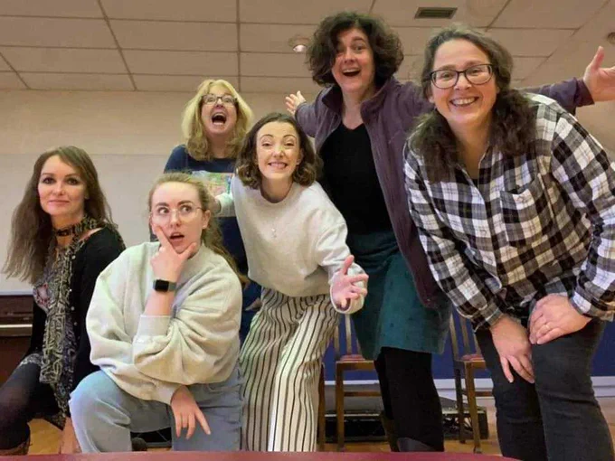 Six women in a bright room posing joyfully for the camera.