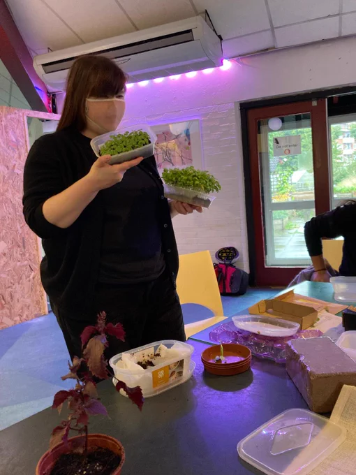 A woman brings dishes containing plants towards a table