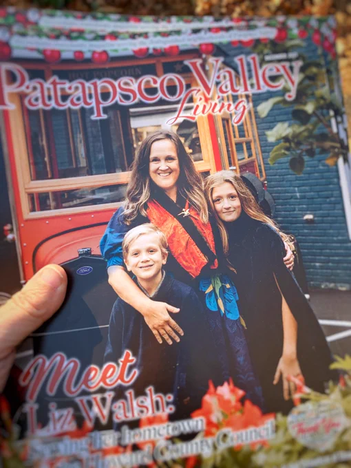 Front cover of the December 2021 issue of the Patapsco Valley Living magazine, fresh out of the mailbox: “Meet Liz Walsh, Serving her Hometown on the Howard County Council.” We shot the photos around Main Street at the end of October, so finding Christmas-y outfits for the two children who grow like weeds was a bit dodgy. Tess is wearing a dark-blue cape, and her auntie did her hair and makeup, so she thinks she’s a super model now. I’m wearing a twenty-five-year-old scarf from a splurge at Nordstrom pinned with a gold bird we bought at Maxine’s—an iconic vintage shop here—after the 2016 flood. Graham is in the front of the three of us, mugging as usual. We look happy.