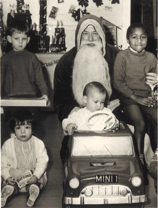 Black and white photograph of man dressed as santa with children sat around him holding toys