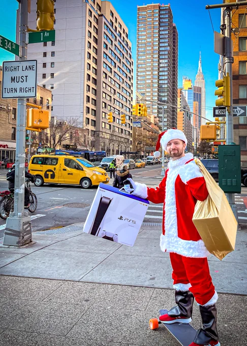 Matt Swider in a Santa Clause outfit with a PS5 and Xbox Series X in hand in NYC