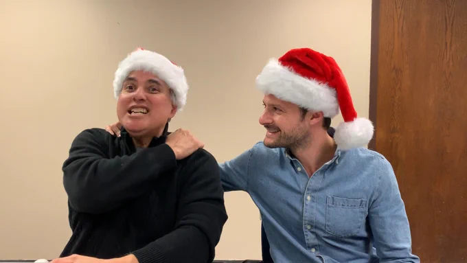 Two men wearing Santa hats share a laugh