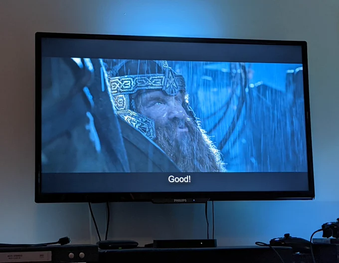 A tv screen showing Gimli at the battle of helms deep, making an enthusiastic face and saying "good!" in response to the uruk-hai using ladders