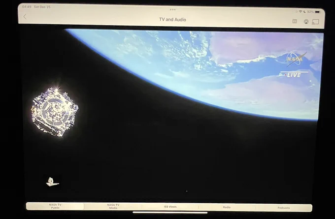 View of JWST as a shiny probe traveling through the black above the rim of the Earth