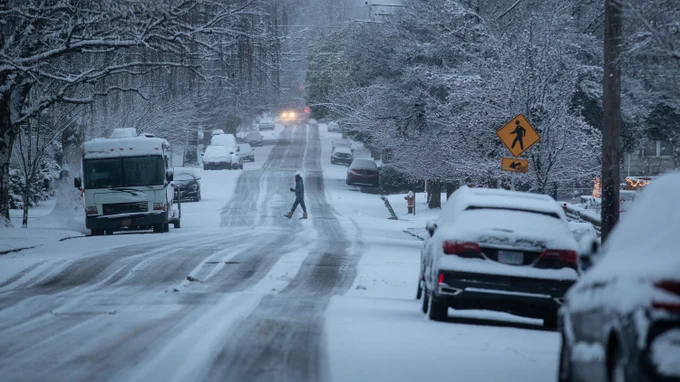 Photo shows an image of a person walking across the street in icy, snowy conditions. 
